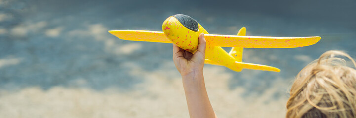 Happy kid playing with toy airplane against old runway background. Traveling with kids concept BANNER, LONG FORMAT