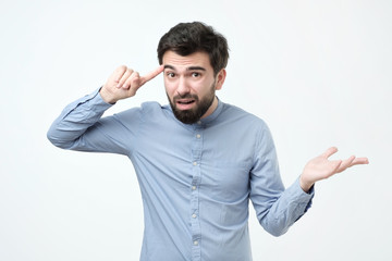 Angry mad young hispanic man gesturing with his finger against temple asking are you crazy....