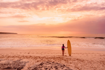 Obraz premium Surfer girl with surfboard at beach. Surfer woman with sunset or sunrise colors.