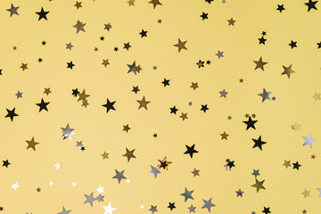 Delicate glitter star confetti on yellow background.