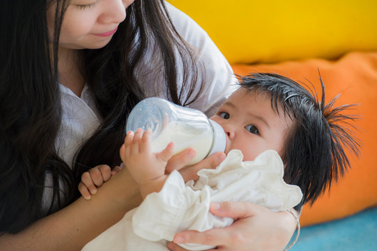 lifestyle candid portrait of young happy and sweet Asian Korean woman feeding her beautiful baby girl with formula bottle at holidays resort as mother nursing daughter