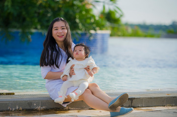 Fototapeta na wymiar young happy and cute Asian Chinese woman playing with daughter baby girl at holidays tropical resort swimming pool enjoying summer holidays trip
