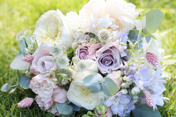 Beautiful wedding bouquet on the background of green grass in the sun. Wedding rings on a wedding bouquet