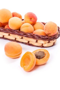 Several of harvested apricots in basket with whole and halved apricots on white background..