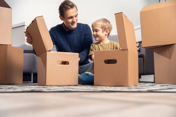 Photo of man and boy sitting on floor among cardboard boxes