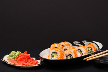 Uramaki California. Sushi rolls and bowl with soy sauce on black background.