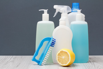 Bottles of dishwashing liquid, brush and lemon on gray background.
