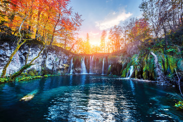 Amazing waterfall with pure blue water in Plitvice lakes. Orange autumn forest on background. Plitvice National Park, Croatia. Landscape photography