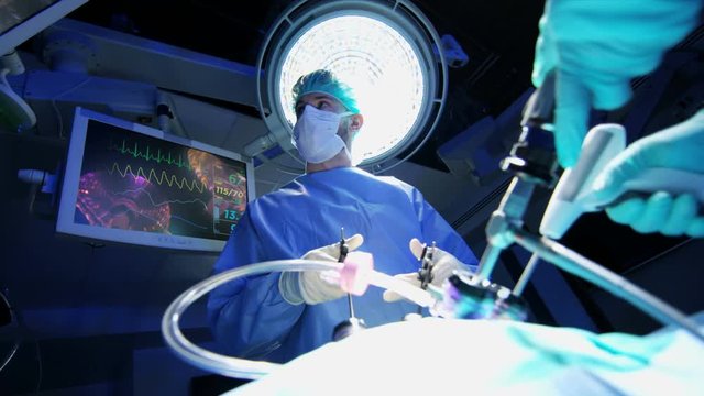 Medical Caucasian hospital specialist team in scrubs training in the operating theatre in laparoscopic surgery using Endoscope technology with monitor equipment 