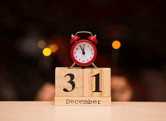 December 31st set on wooden calendar with red alarm clock on dark blurred background.