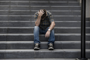 young sad and desperate man sitting outdoors at street stairs suffering anxiety and depression...