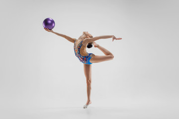 The teen female little girl doing gymnastics exercises with ball on a gray studio background. The...