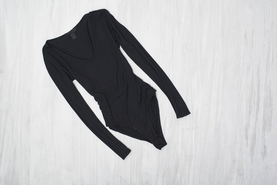 Black bodysuits with sleeves on a wooden background. Fashionable concept