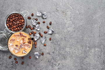 Chocolate, vanilla, caramel or cinnamon iced coffee in tall glass. Cold brewed iced coffee in glass and coffee beans in glass jar on grey concrete background. Top view with copy space for text.