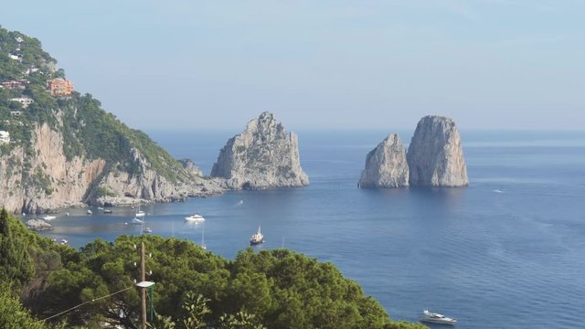 Famous sea stack Faraglioni and coastal mountains. Watercrafts float near Capri, Italy