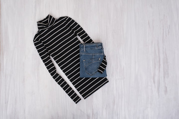 Black striped turtleneck and jeans on wooden background. Fashionable concept