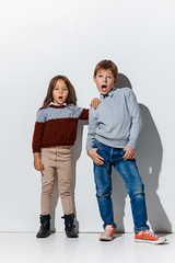 The portrait of cute little kids boy and girl in stylish jeans clothes looking at camera against white studio wall. Kids fashion and happy emotions concept