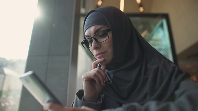 Pensive female in traditional Muslim clothing chatting on phone, online banking