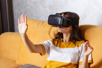 Cute long-haired girl in pullover wearing a virtual reality headset while sitting on the yellow...
