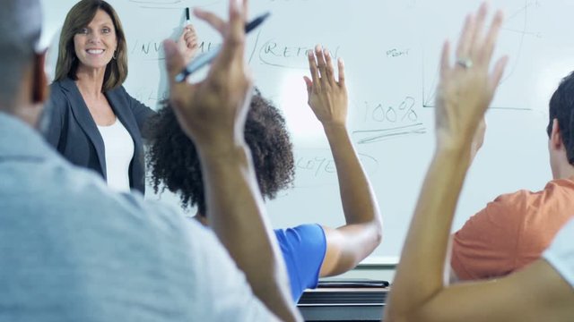 Smart Caucasian American female tutor teaching mature university students in modern classroom 
