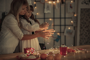 Mother and her daughter in a cook cap have a fun and sprinkle flour on the table.