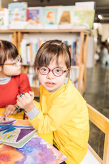 Cute dark-eyed girl with Down syndrome wearing bright yellow sweater