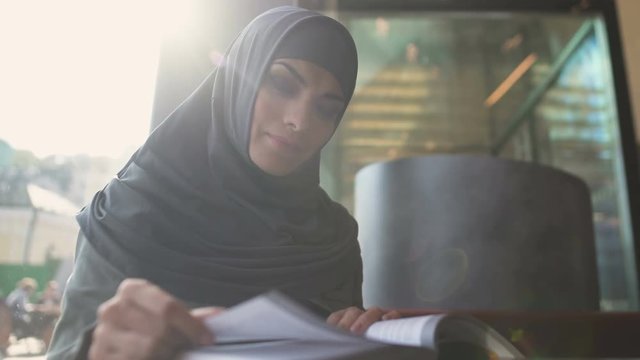 Motivated Muslim female student reading book in cafe modern education literature