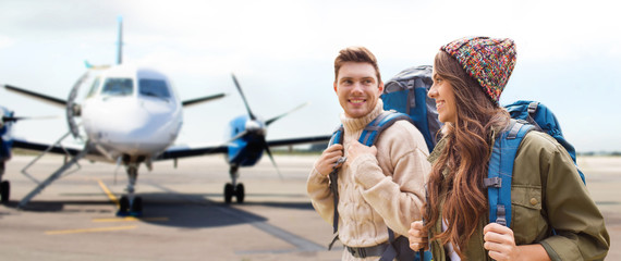 travel, tourism and people concept - couple of tourists with backpacks over plane on airfield background