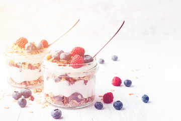 Two jars with tasty parfait made of granola, berries and yogurt on white wooden table. Shot at angle. Toned image with copy space.