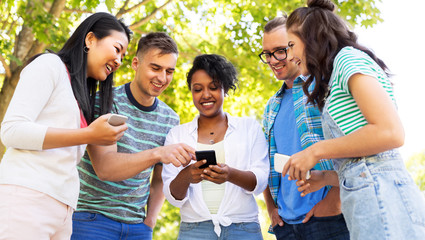 friendship, technology and international concept - group of friends with smartphones at summer park
