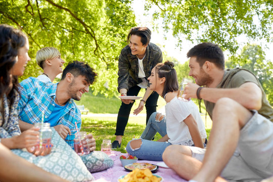 friendship and leisure concept - group of happy friends with non alcoholic drinks and food at picnic in summer park