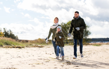 family, leisure and people concept - happy mother, father and little daughter running along autumn beach