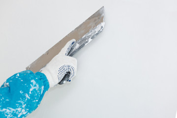 Hand with a spatula in the process of leveling the raw plaster.