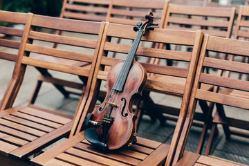 Violin on wooden chair in garden. Preparation for concert or perfomance. String musical instrument...