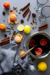 Mulled wine in aluminum casserole on gray wooden table. Christmas or winter warming drink. Ingredients: wine, lemon, cinnamon sticks, anise, cardamon, raisin. Top view. Flat lay