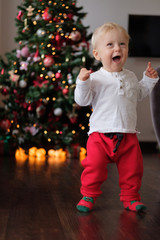 Christmas portrait of a happy baby in Christmas pajamas with a deer on the background of the Christmas tree