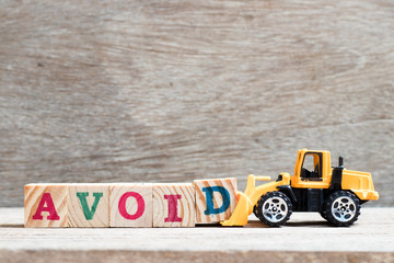 Toy bulldozer hold letter block d to complete word avoid on wood background