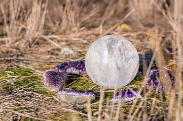 White Quartz ball surrounded by amethyst crystals laying in the grass