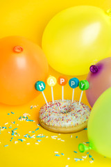 birthday cake, poured with icing and sprinkled colorful sprinkles with the inscription HAPPY with candles on a yellow background, surrounded by balloons