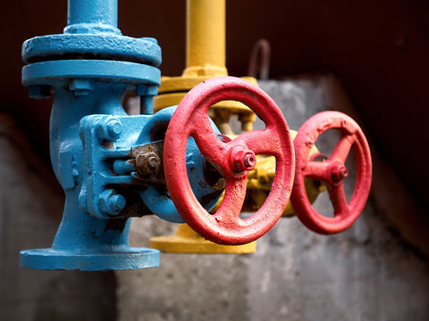 Two drain valves blue and yellow with red steering wheels over background of tank at chemical plant