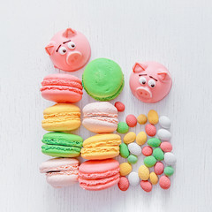 Marzipan in the shape of the symbol of the new year - pink pig, sweet delicate macaroons, marshmallows, peanuts in sugar pastel colors on a light background with space for text