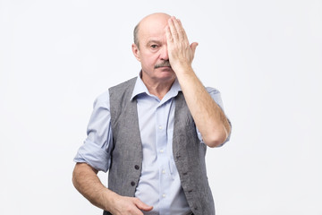 Serious senior man covering one eye while having his eyes tested. Vision examination at old age...