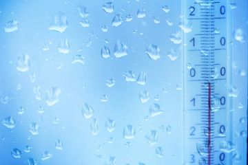 Snow melts on the window with blue glass. Water drops.