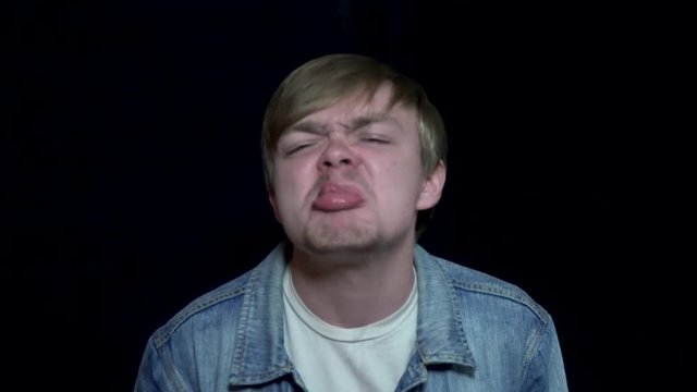 Man showing his tongue. Young man angrily grimaces and out tongue. Human facial expressions and emotions. Black isolated background
