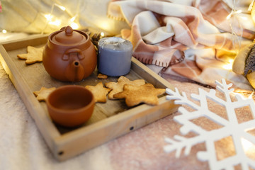 Wooden serving tray with brown ceramic kettle, steaming hot drink mug in a cozy home interior. Food, drinks, toy, gingerbread cookies. Concept enjoying autumn, winter mood, tea time, Christmas holiday