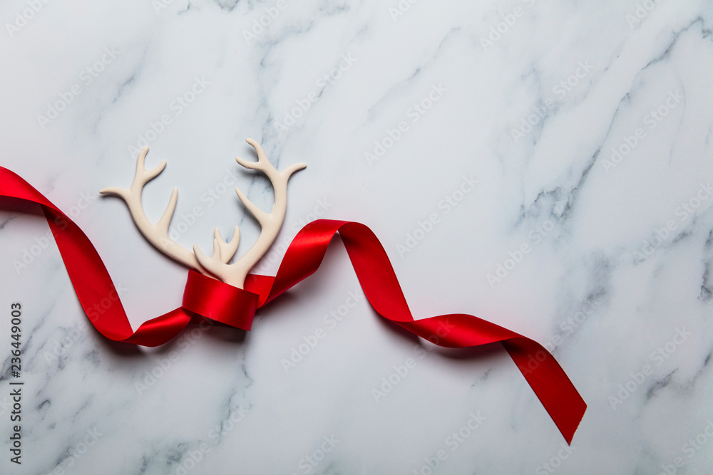 Wall mural Festive reindeer antlers and red ribbon on a marble background