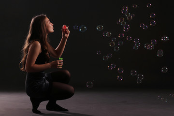 young woman blowing bubbles against dark wall