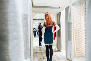 Young beautiful girl trying on new green dress in the fitting room in boutique.