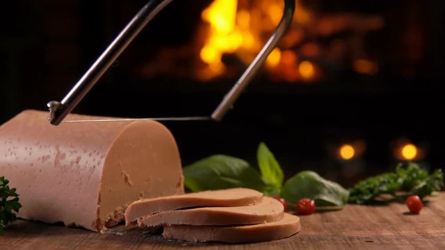 Special knife cuts a piece of foie gras on a wooden board against the background of a burning fireplace
