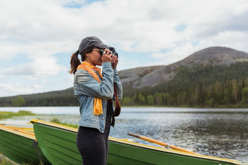 Finland, Lapland, woman taking picture with a camera at the lakeside
